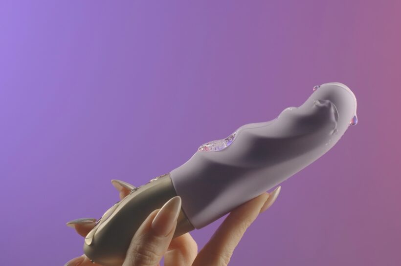 Faloimitator.Creative.A small gray vibrator on a gentle background in the hand on which grease is