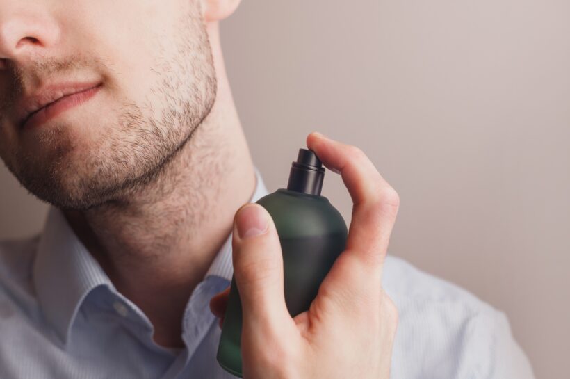 Handsome unshaven man applying perfume on neck, closeup.