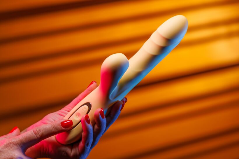 A female hand with a sensual red manicure presses the button on the vibrator.