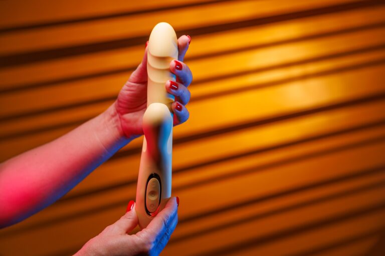 A vibrátorozás modern technikái A woman with sexy red nails displays a yellow vibrator turning it in her hands.