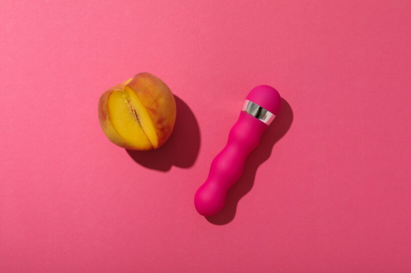 Pink vibrator with a peach on a pink background.