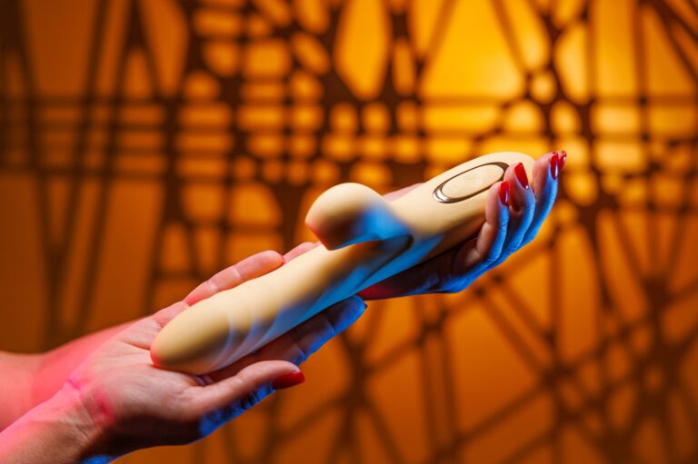 A vibrátorok történeti gyökerei A womans hands with a sexy red manicure rotate a yellow clitoral vibrator.
