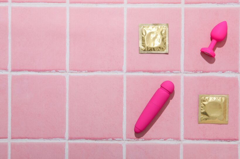 Condoms, butt plug and vibrator on a pink background, place for text